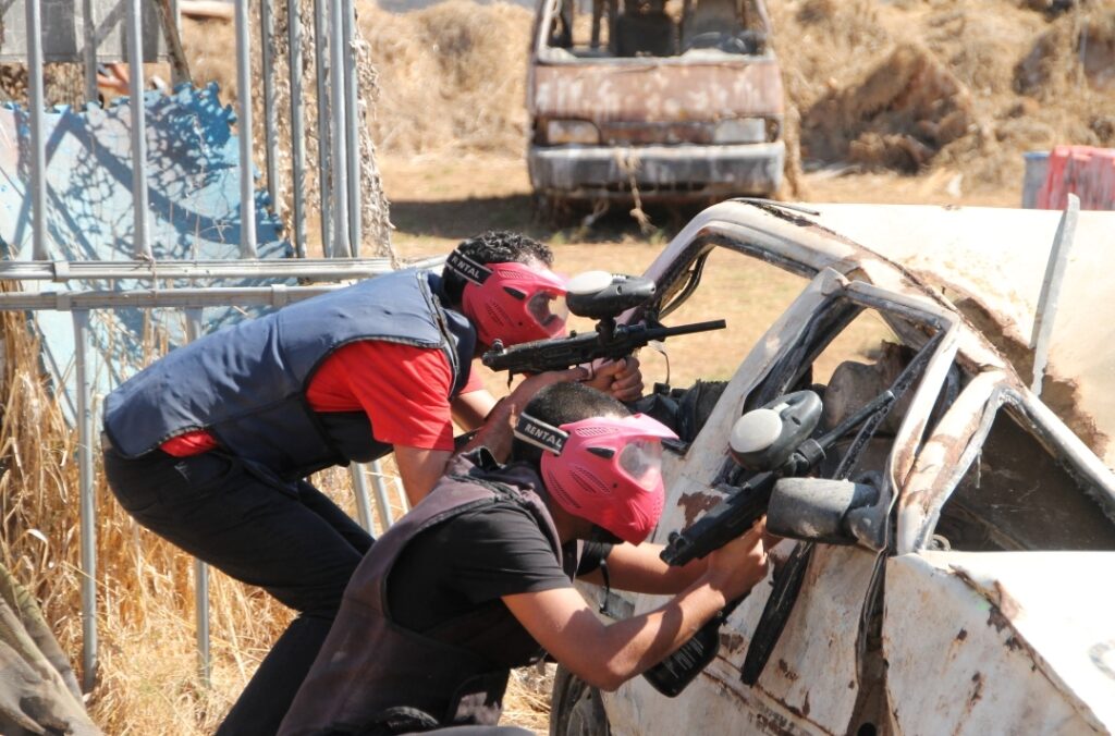 שני שחקני פיינטבול יורים ממחסה של רכב נטוש בשטח
